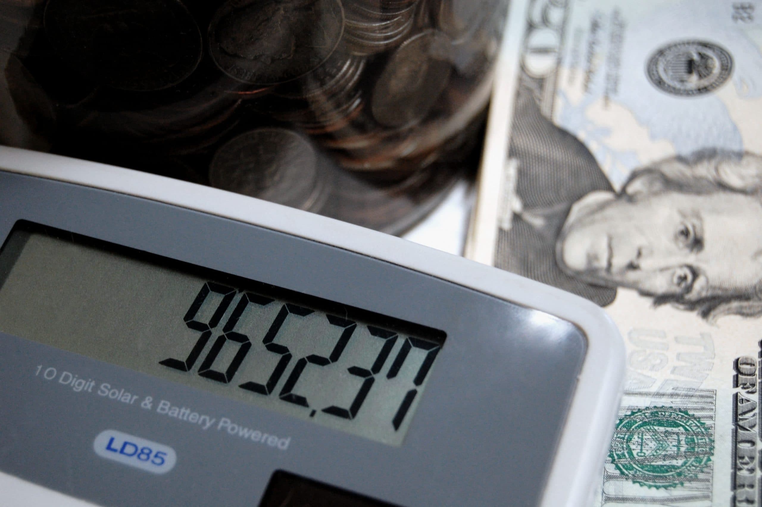 Coins in a jar, dollar bills, and a digital calculator showing $45,523.70, representing financial management.