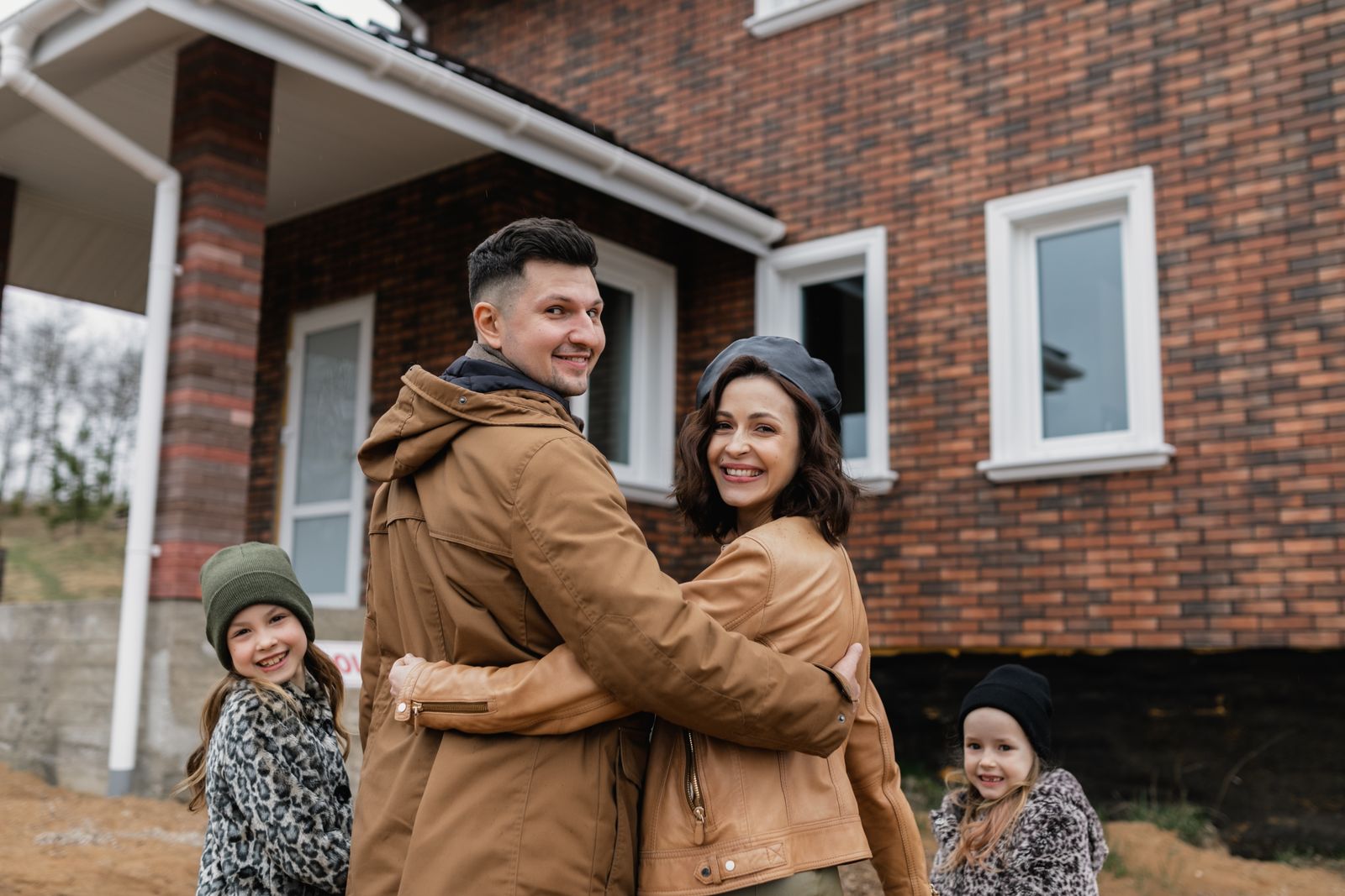 A family standing proudly together in front of their brick home
