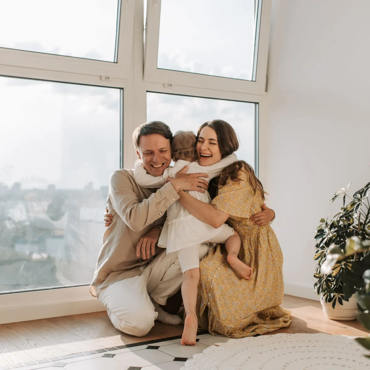 A family sharing a warm hug by a sunny window inside their home