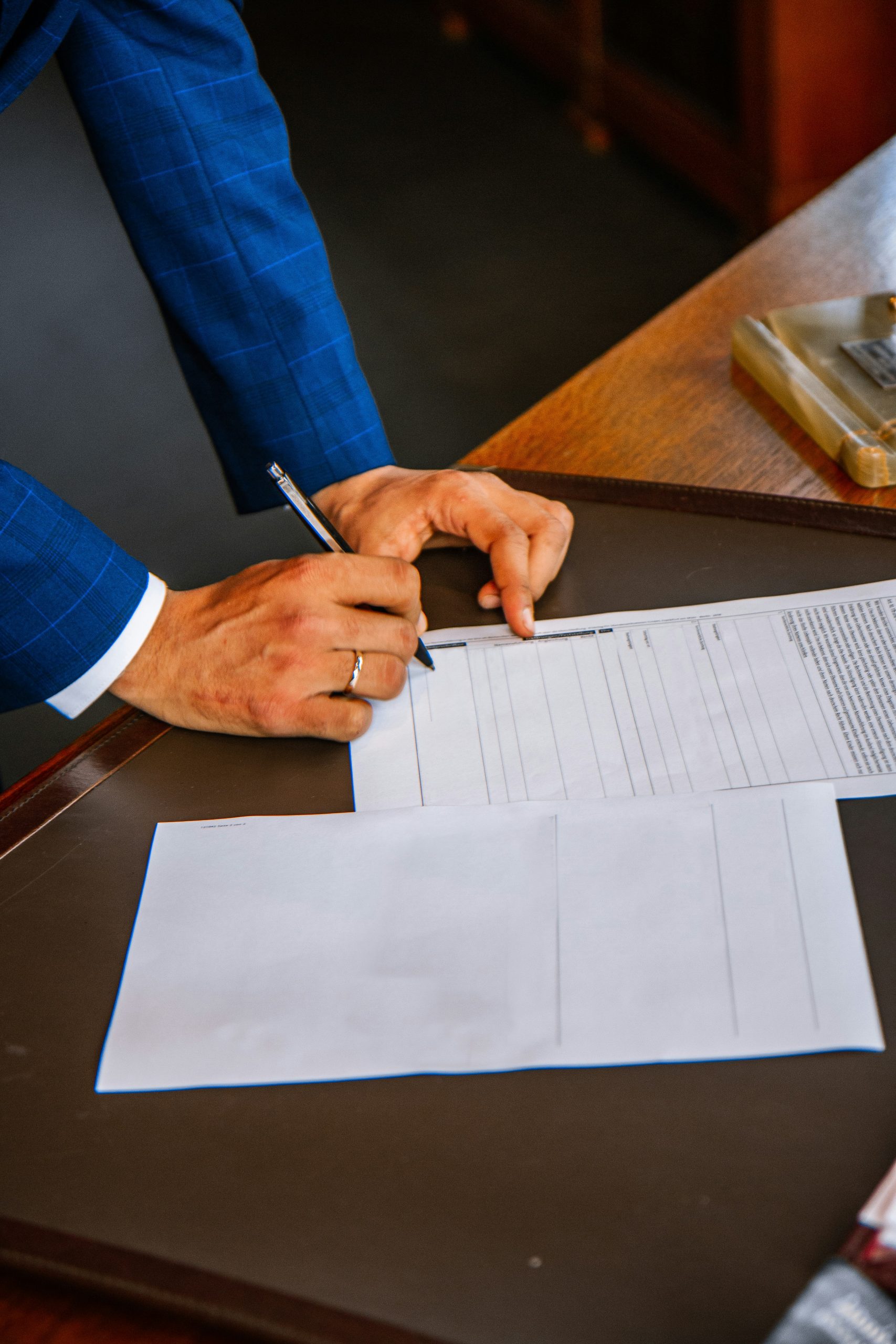 A person in a blue suit signs documents at a tidy desk with Foreclosure Attorneys Long Island & NYC.