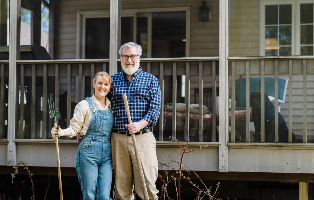 A happy older couple smiling together on the porch of their home with gardening tools