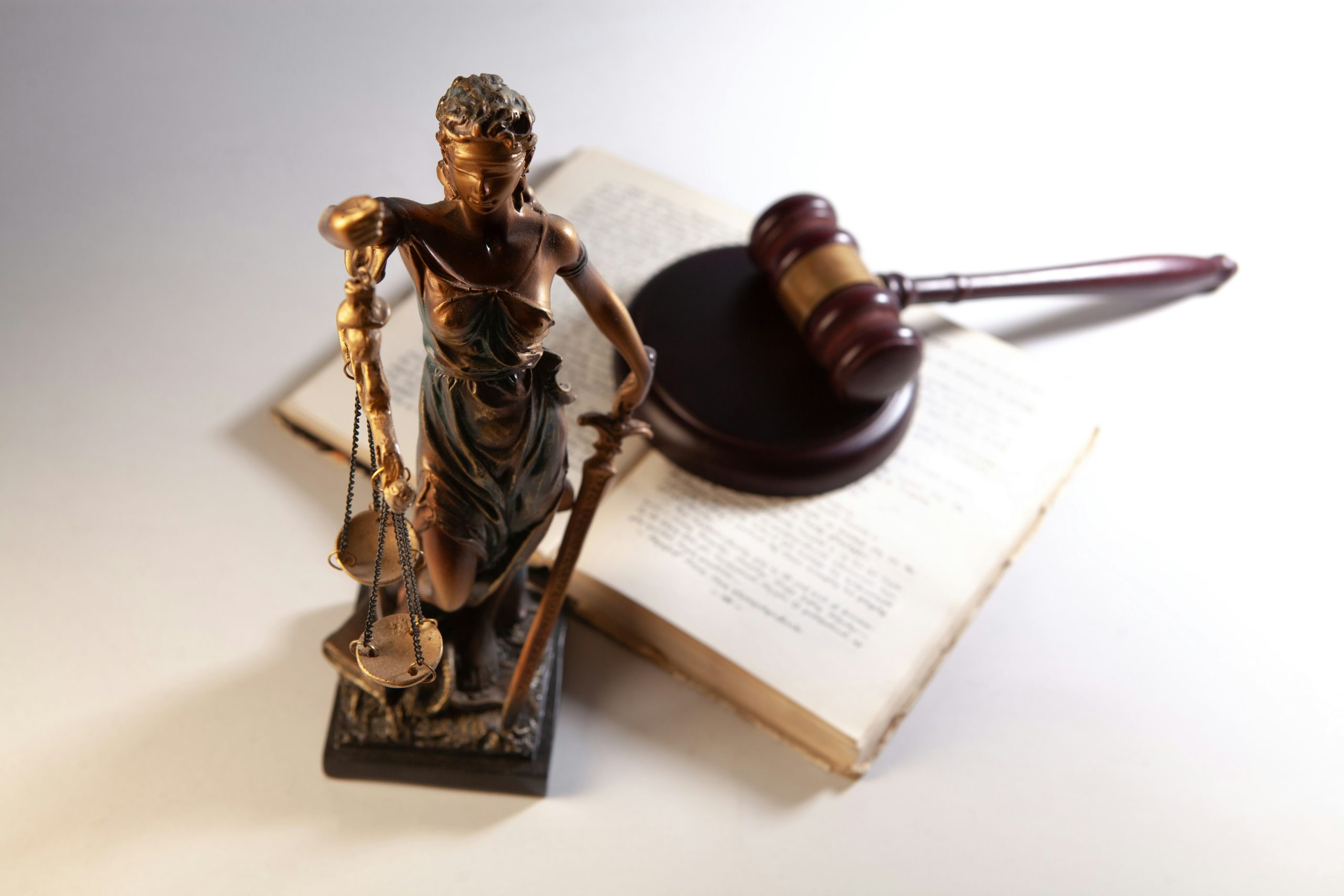A bronze Lady Justice statue stands by a gavel and law book, symbolizing Foreclosure Attorneys NYC.