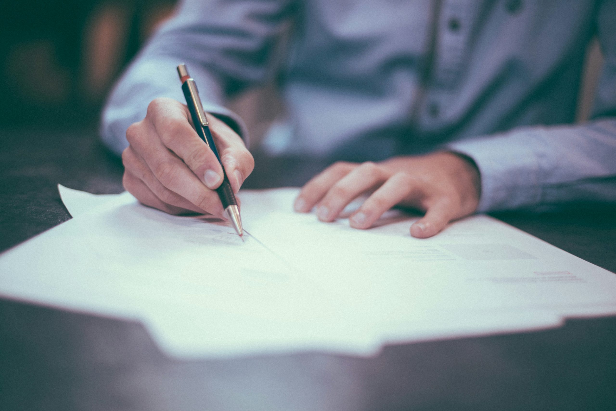 A person in a blue shirt writes at a desk, reviewing Bankruptcy Attorneys Long Island & NYC documents.