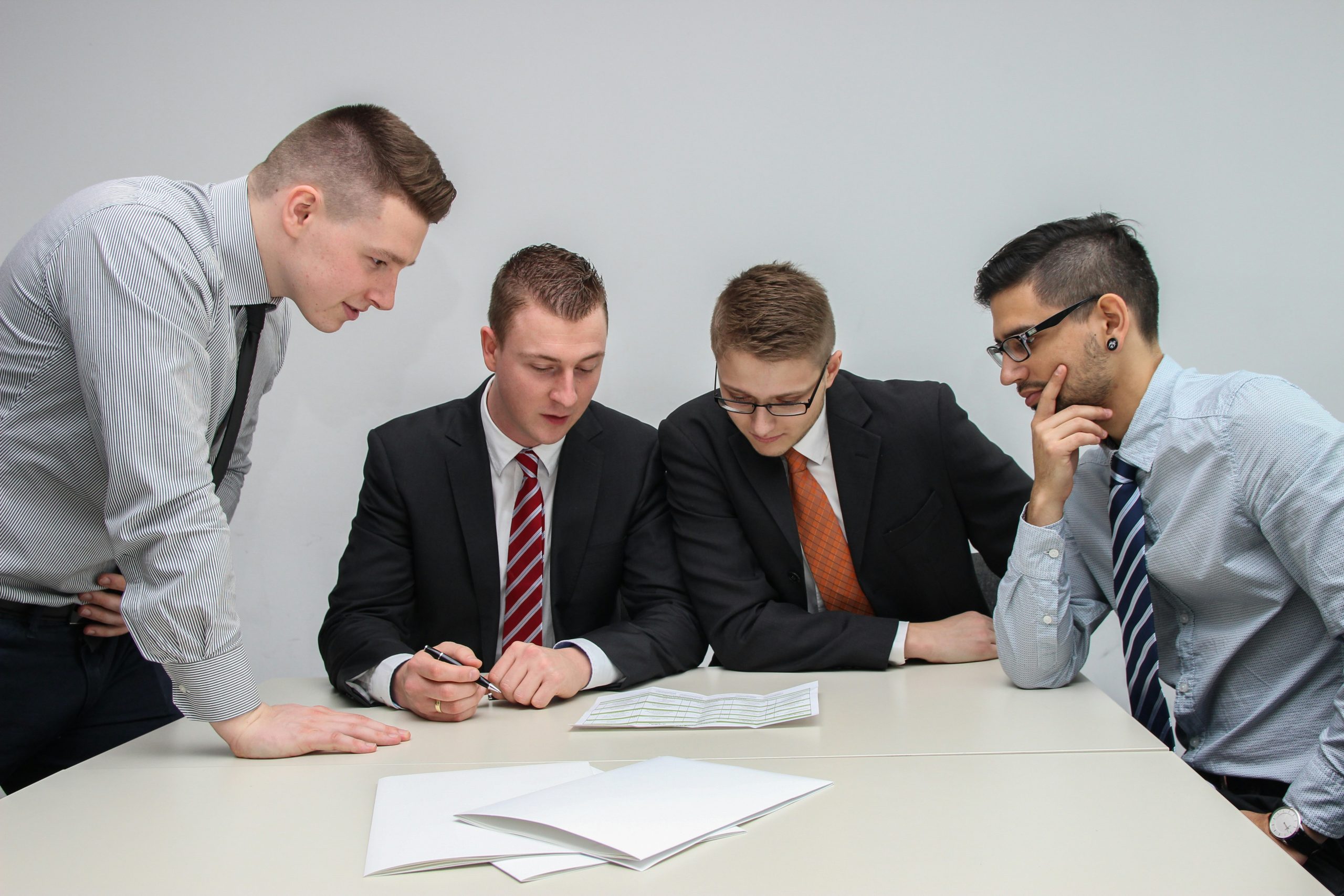 Four men in business attire, likely Bankruptcy Attorneys Long Island & NYC, review papers at a table.