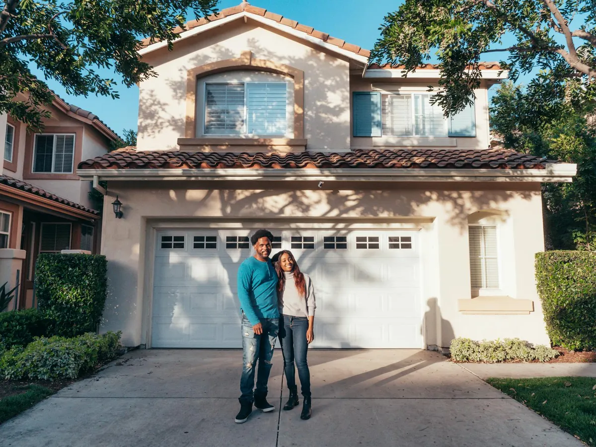 A couple standing proudly in front of their suburban home