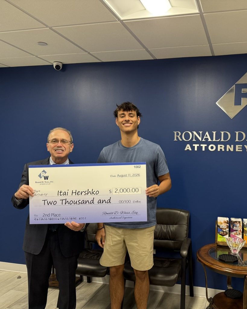 Attorney Ronald D. Weiss presents Itai Hershko with a large ceremonial check for $2,000 for second place in the Spring 2026 scholarship essay contest, in the firm's Long Island office.